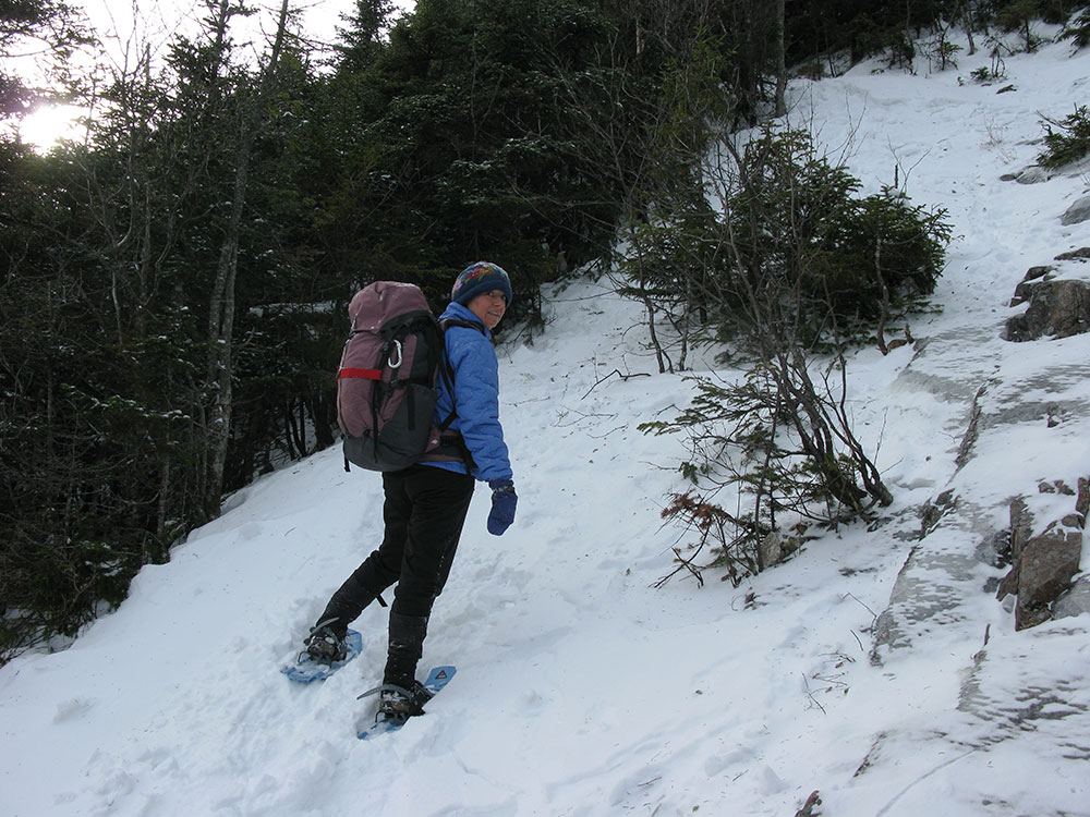 hiker snowshoeing up a steep section of snowy trail