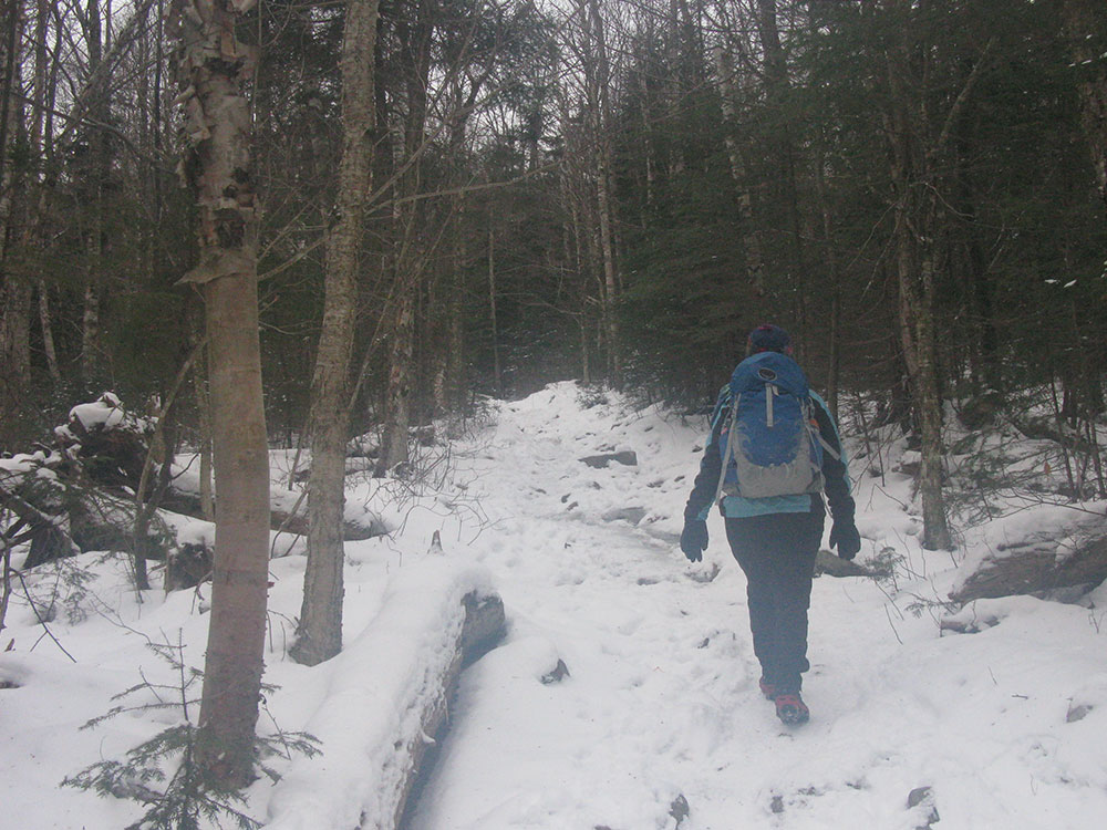 hiker walking up trail covered in a shallow layer of snow