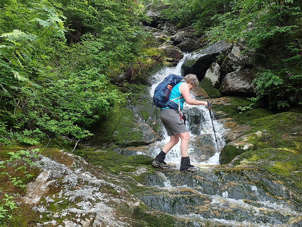 hiker crossing slippery stream above a waterfall