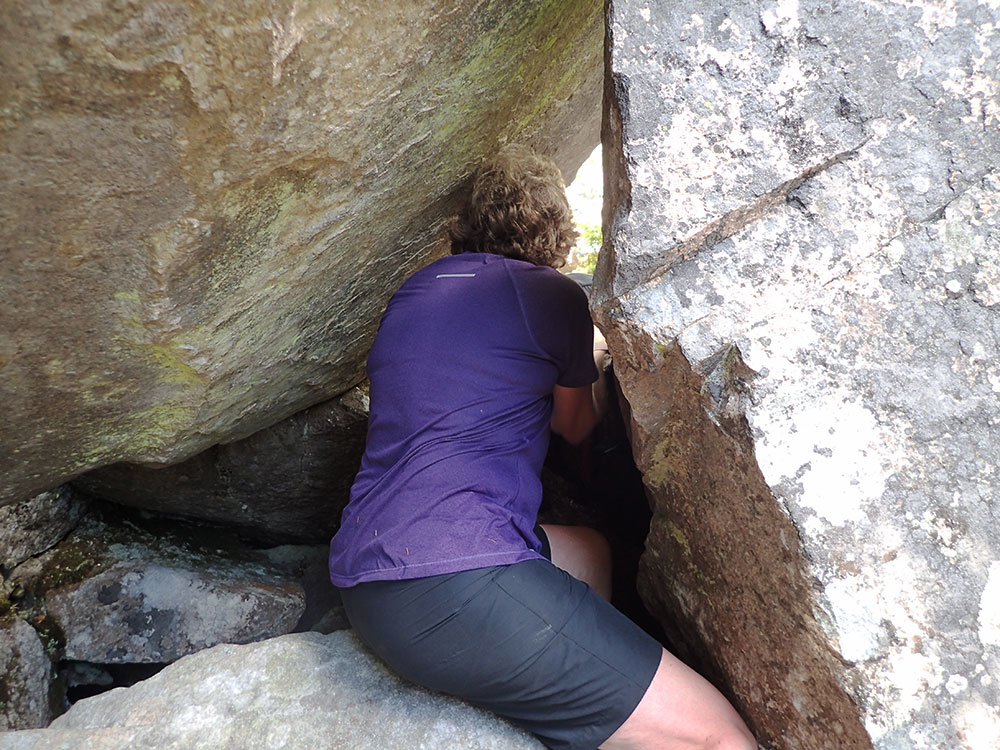 hiker squeezing between two boulders