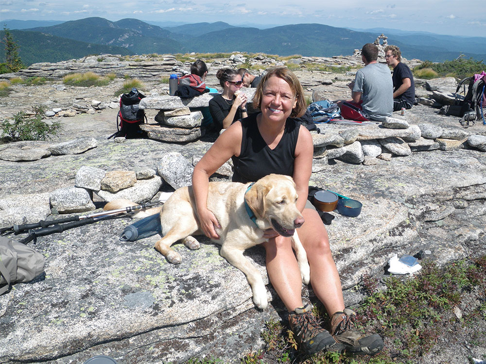 Hiker and yellow lab lying in her lap on top of the Baldface Ledges