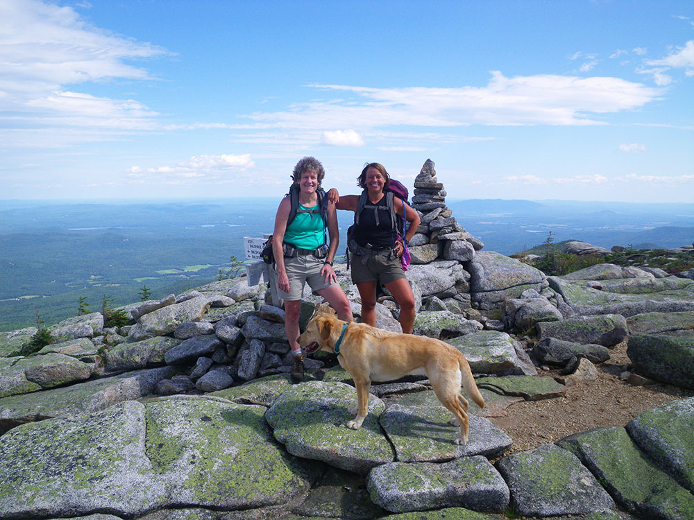 two hikers and yellow lab posing at the summit