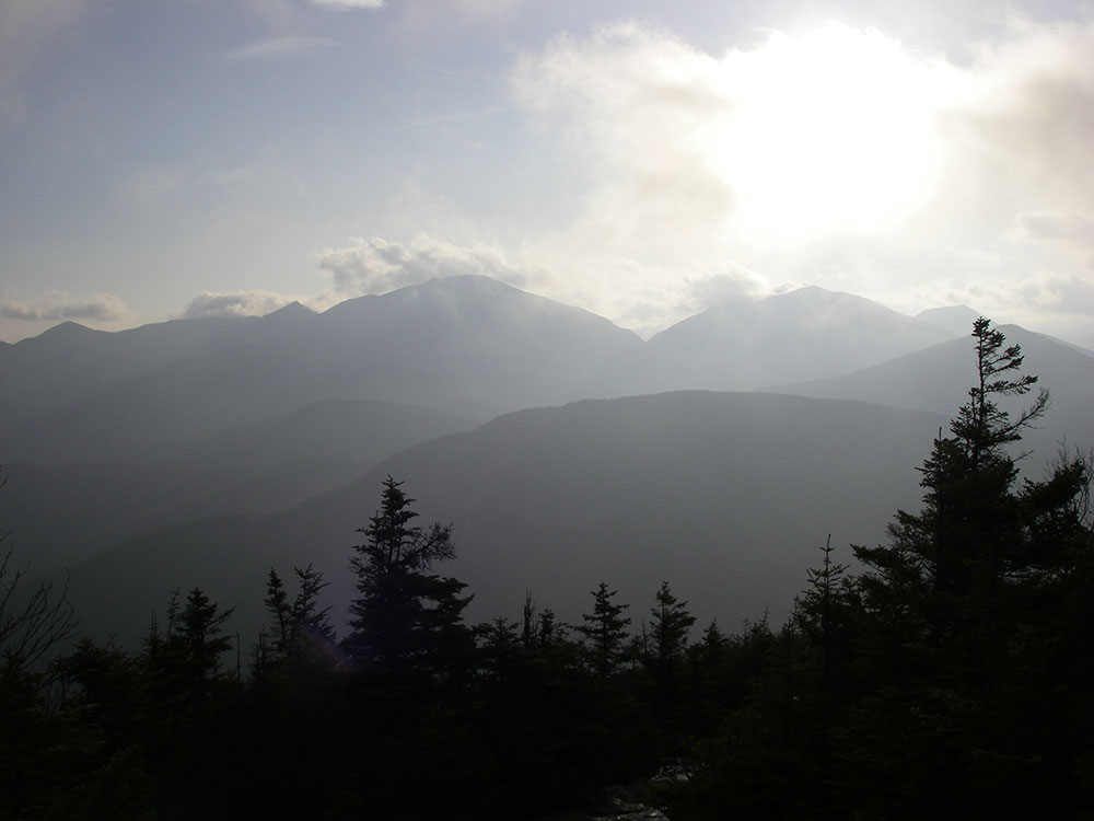 sun through clouds as the day clears with mountains in the distance