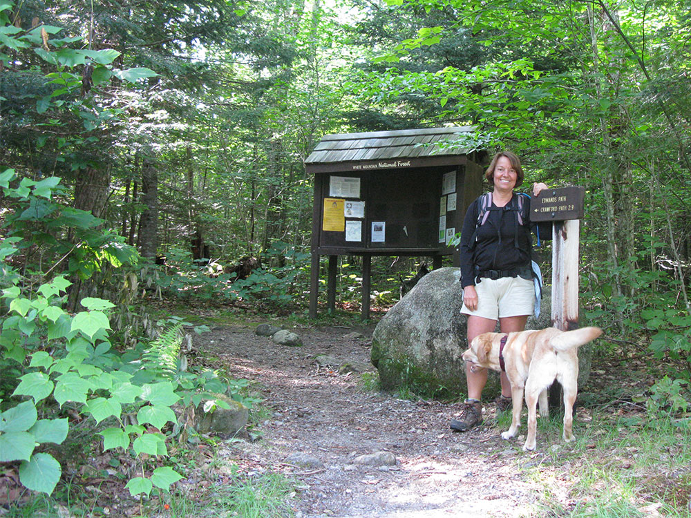 Nancy and Dejah hiker and yellow lab at the trailhead sign