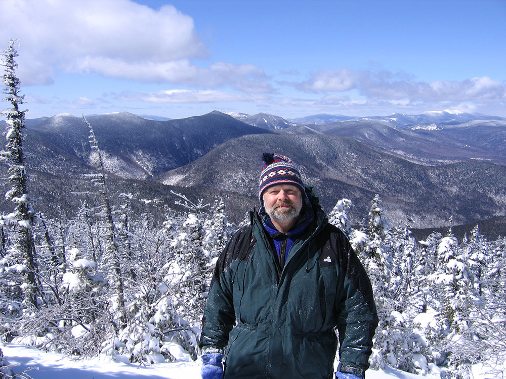 hiker posing at viewpoint of distant snow-covered peaks