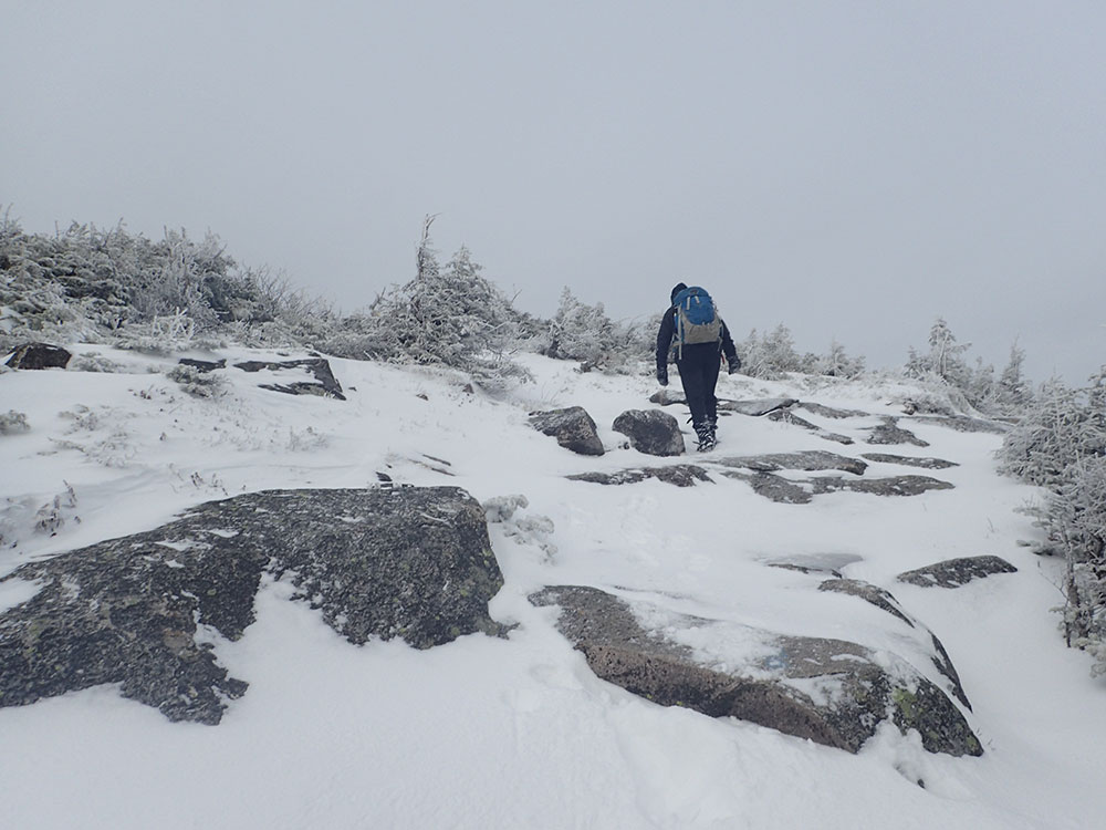 hiker walking in grey clouds on snowy trail